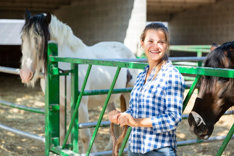 Femme heureuse éleveur de chevaux près d'une écurie